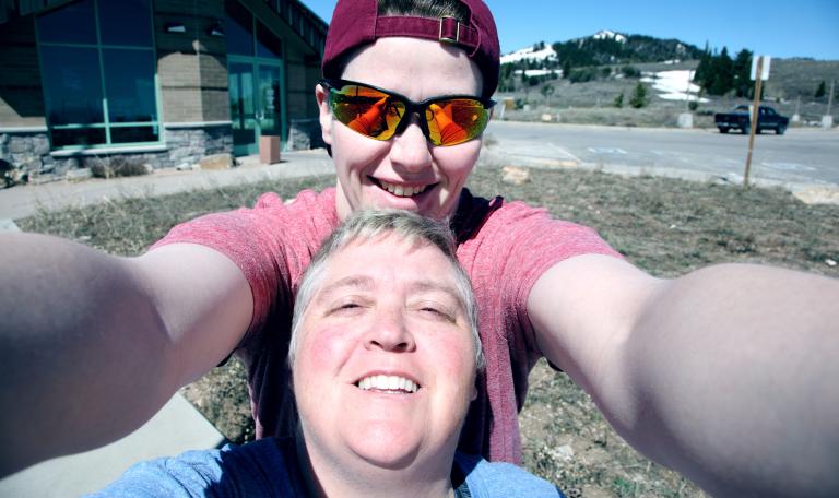 Two ladies taking a selfie. One is wearing a headscarf and sunglasses the other has short grey hair.