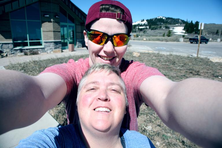 Two ladies taking a selfie. One is wearing a headscarf and sunglasses the other has short grey hair.