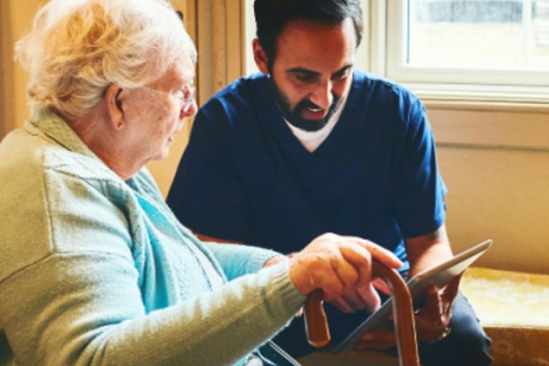 Male carer and older woman with a hand held device